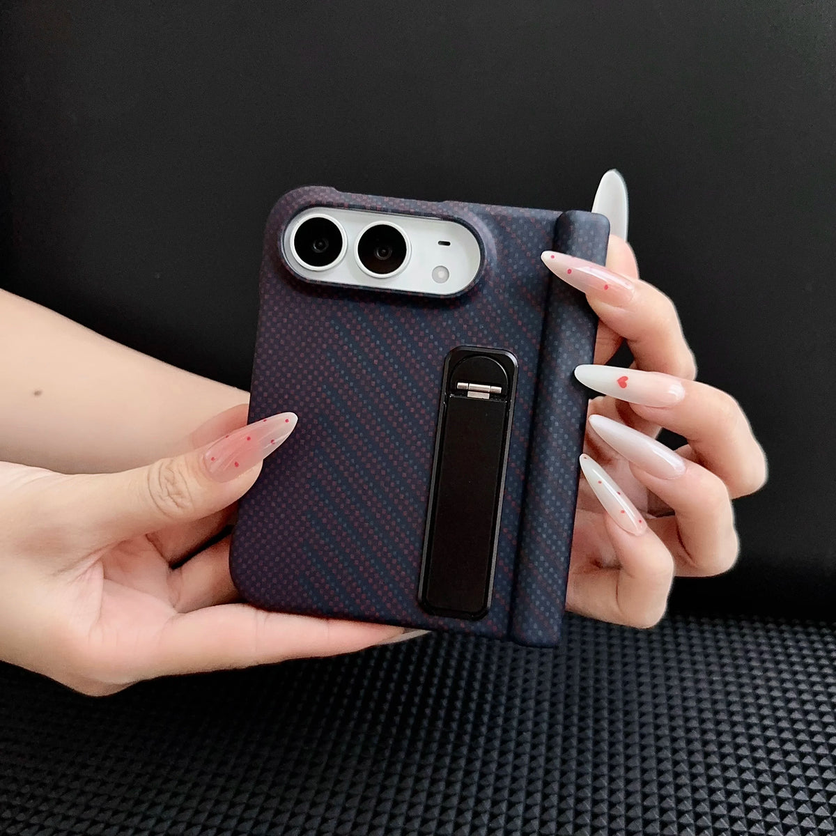 Kevlar-weave case with metal stand on a closed iPhone Duo, held in hand